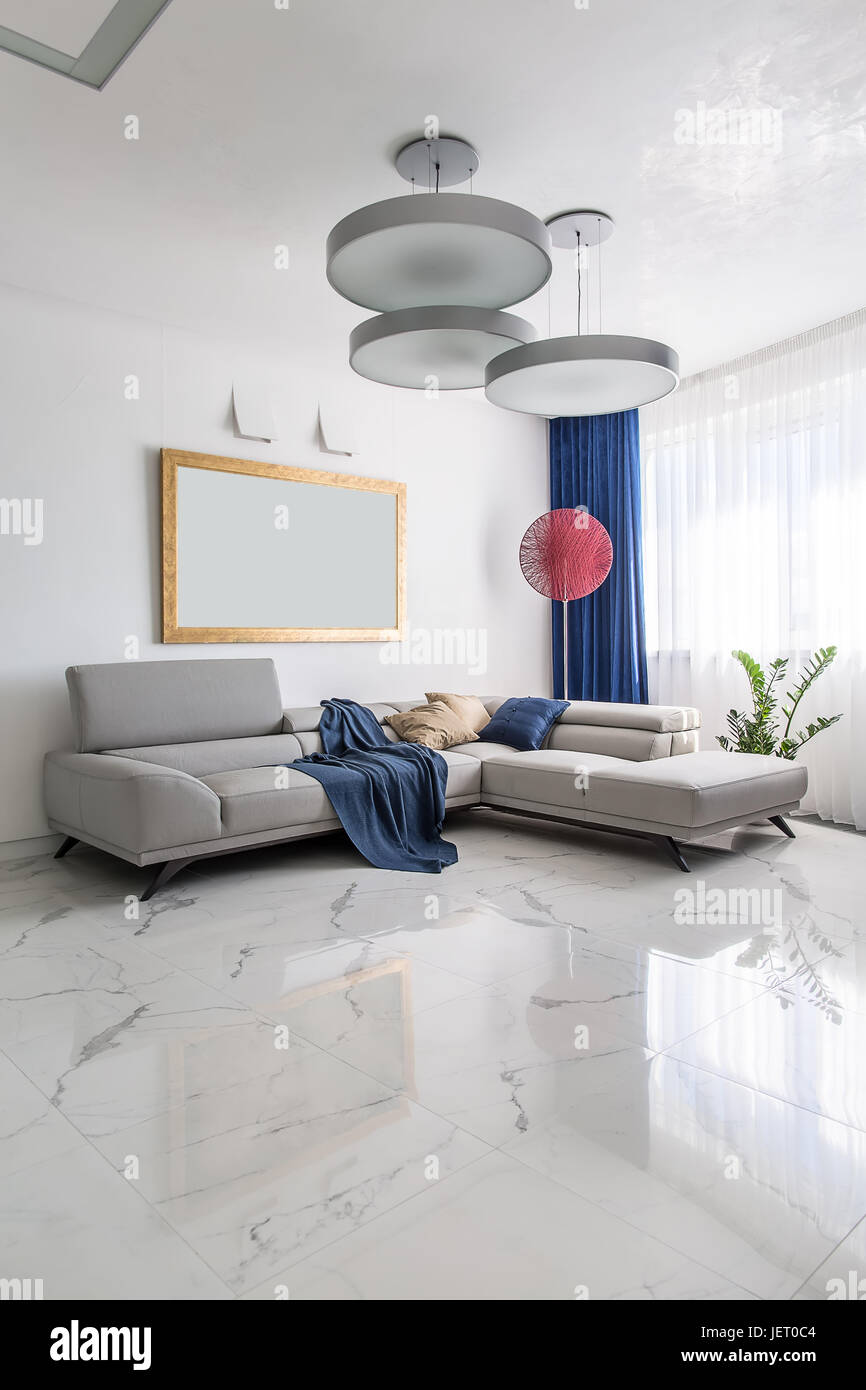 Modern room with white walls and light tiled floor. There are gray sofas  with multicolored pillows and a blue plaid, fancy red lamp, hanging round  lam Stock Photo - Alamy