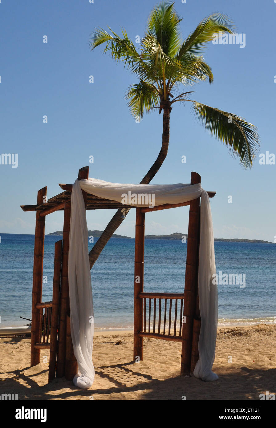 Wedding Arbor draped in white fabric located on the beach with a palm tree behind it. Stock Photo