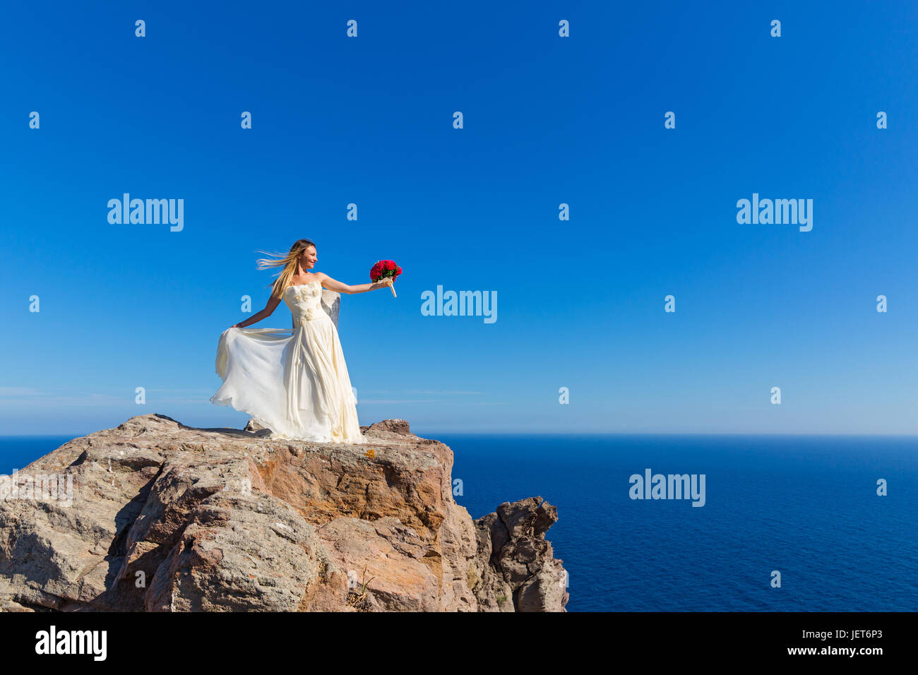 Beautiful woman in white dress stands on a high cliff near the sea ...