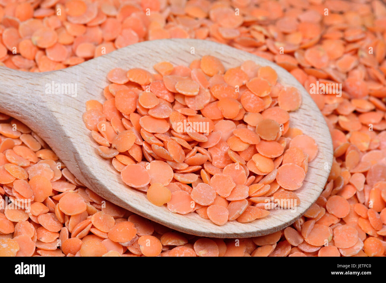Many red lentils in a wooden spoon close-up Stock Photo