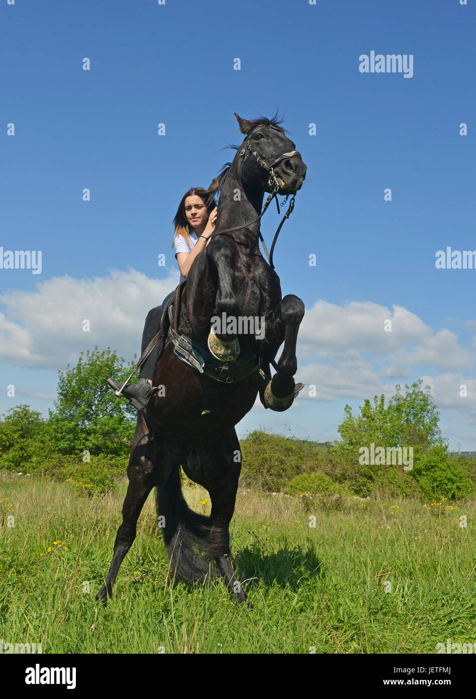 young riding girl and her black stallion in nature Stock Photo