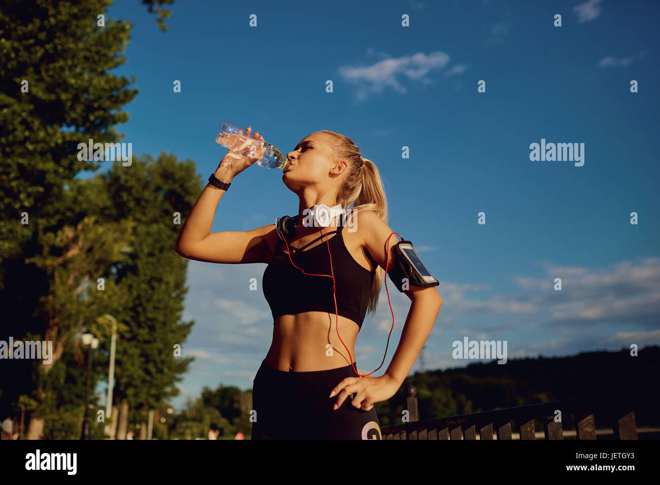 Girl runner drinks water from a bottle in the park. Stock Photo