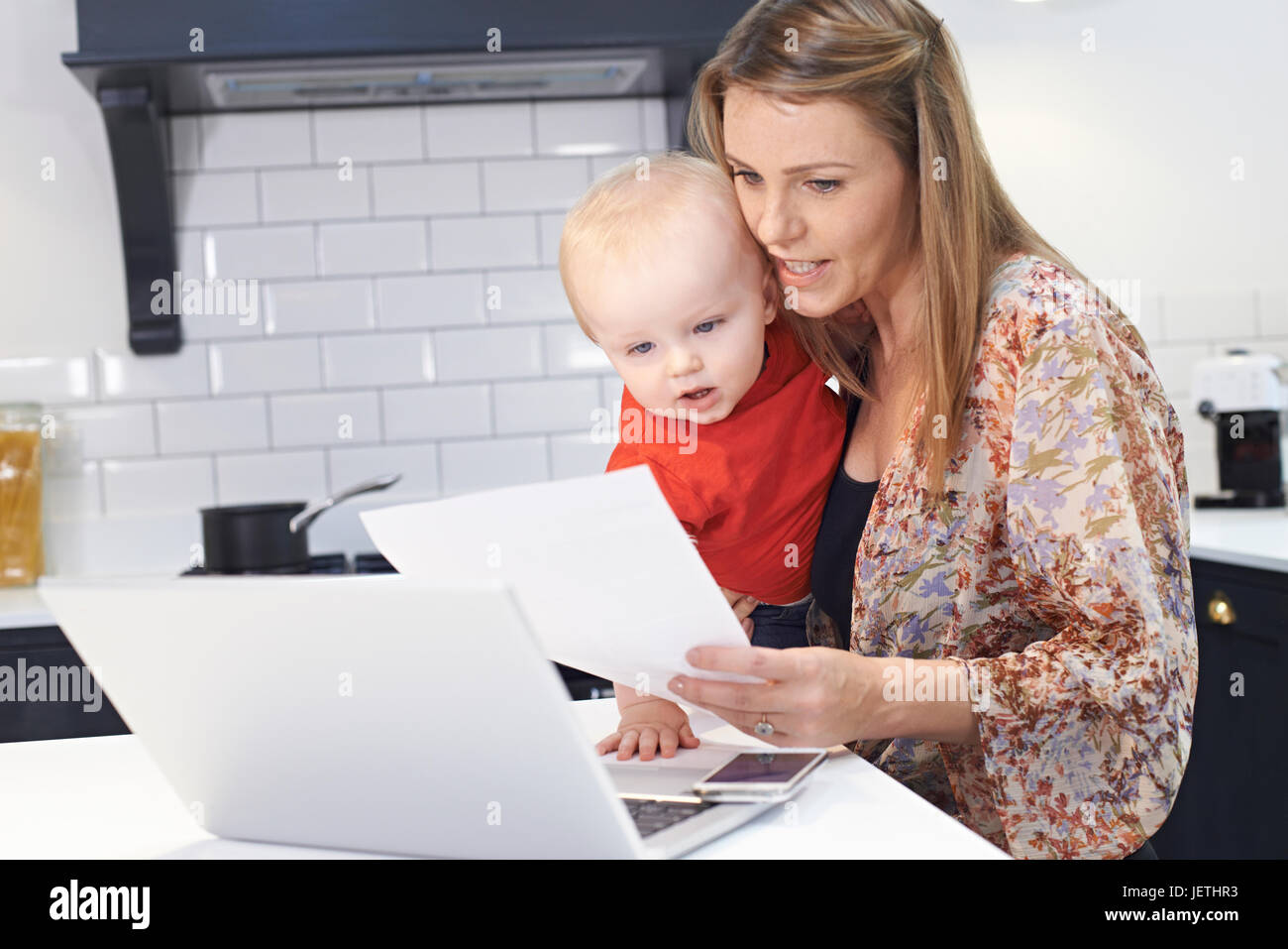 Busy Mother With Baby Coping With Stressful Day At Home Stock Photo