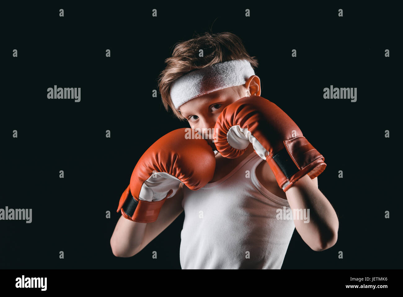 boy obscuring face with boxing gloves isolated on black, active kids concept Stock Photo