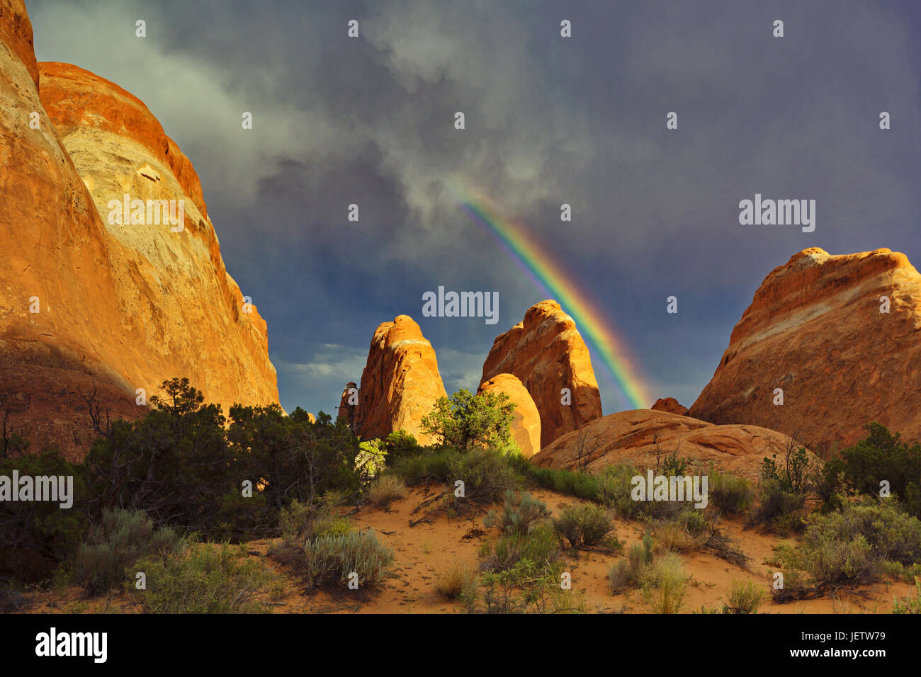 Suggestive image of rainbow bursting from storm clouds as sunlight graces red hues of rocks in Utah. Positive beauty in nature and concepts of hope an Stock Photo
