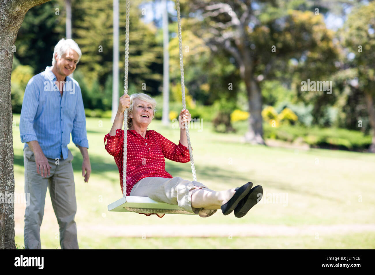 Senior man pushing his partner on swing Stock Photo