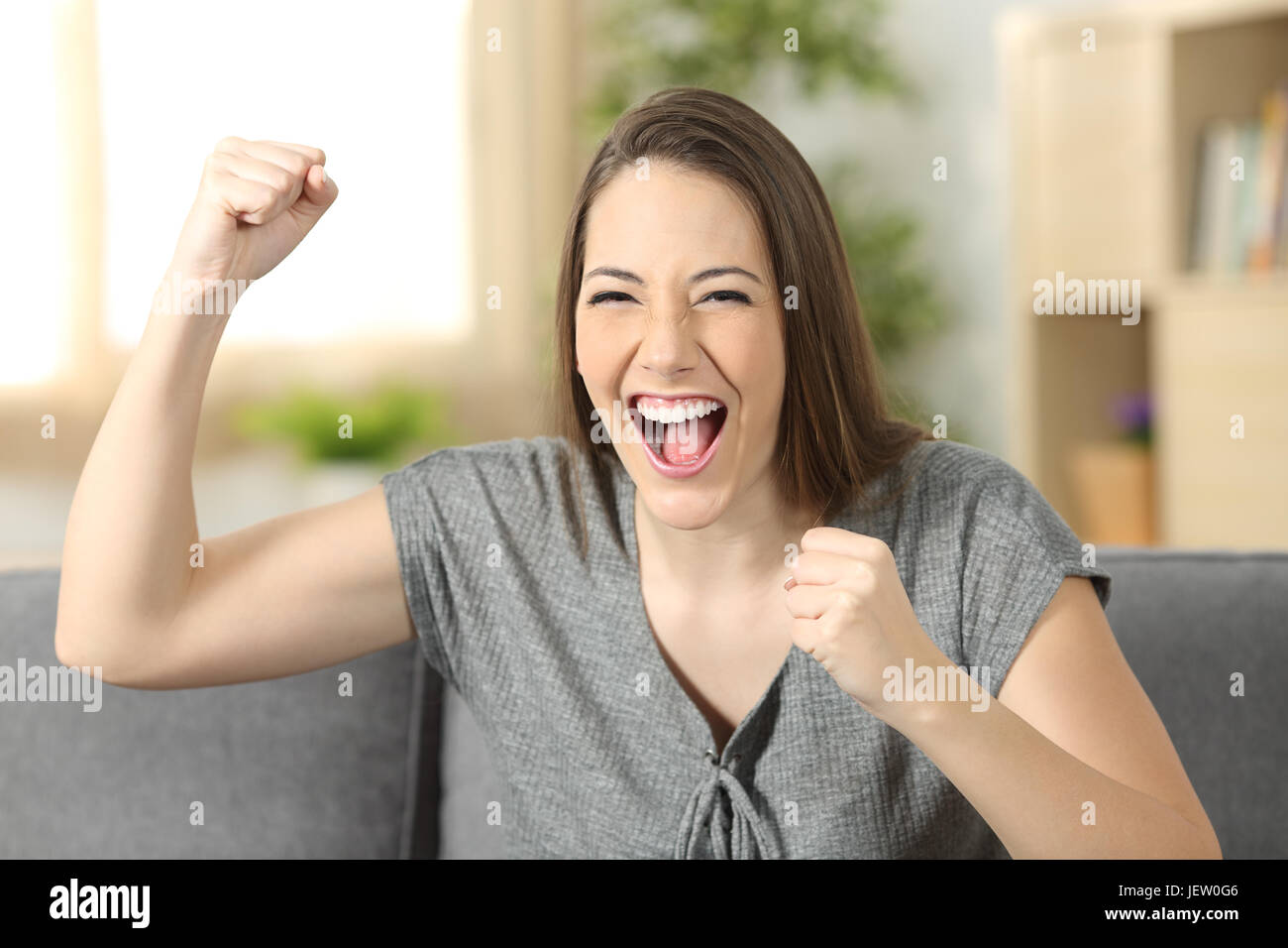 Excited Woman Looking At You Sitting On A Sofa In The Living Room At