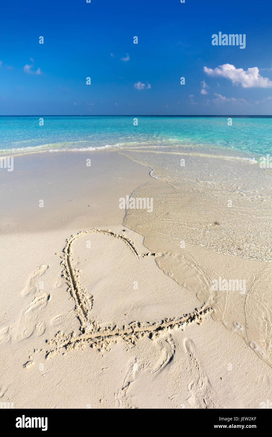 Waves wash away a heart drawn on sand of a tropical beach. Concept of romantic love, broken heart etc. Stock Photo
