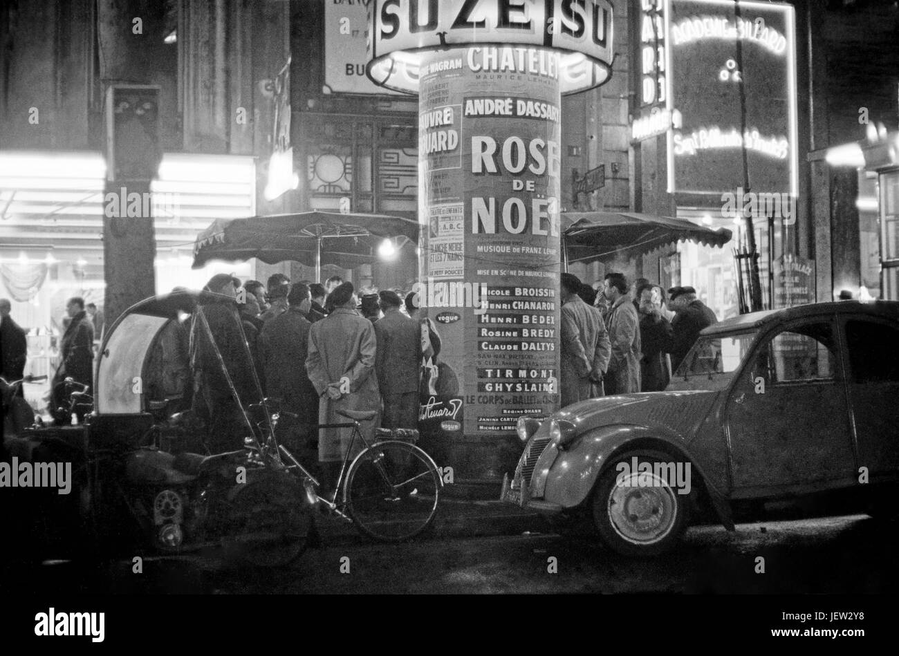 Nightlife in Paris: pedestrians are gathered around an typical Parisian advertising column ('Colonne Morris').  December 1958 Photo Michael Holtz Stock Photo