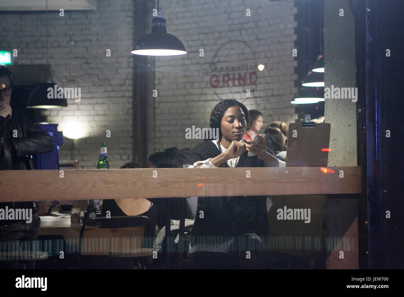 LONDON, ENGLAND - JULY 12, 2017 A black girl in a cafe looks at her phone Stock Photo