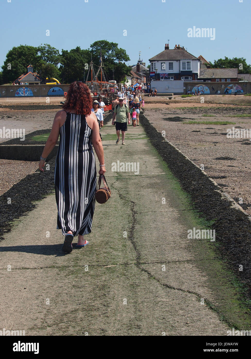 People walking along Queenborough Harbour causeway. Woman prominent in long stripey dress. Stock Photo