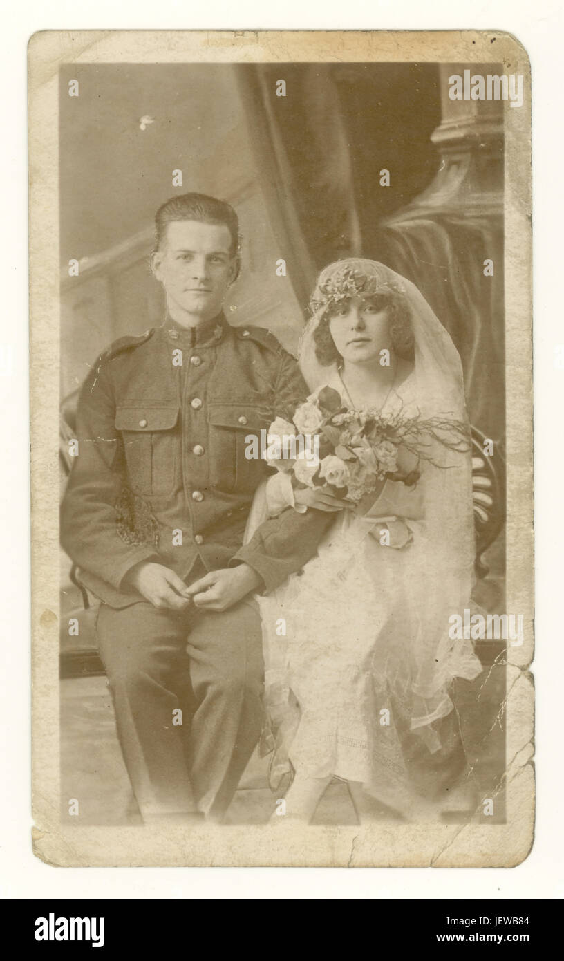 Original WW1 era faded sepia postcard studio portrait of attractive wedding couple, soldier husband in army uniform, wife wearing beautiful veil and headdress, carrying a bouquet, circa 1918, England, U.K. Stock Photo