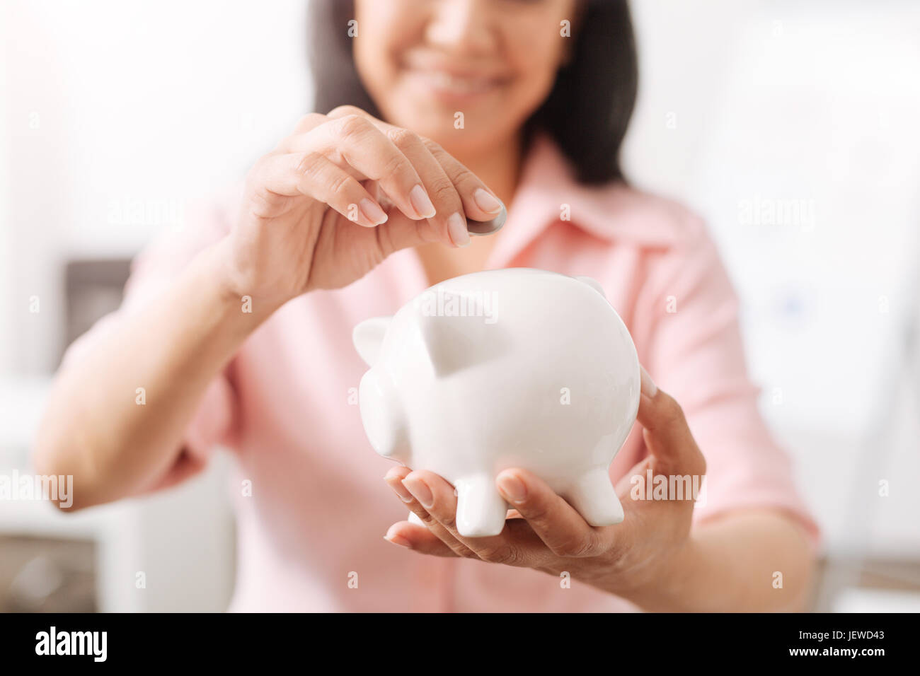 Positive woman putting coins into a piggy bank Stock Photo - Alamy