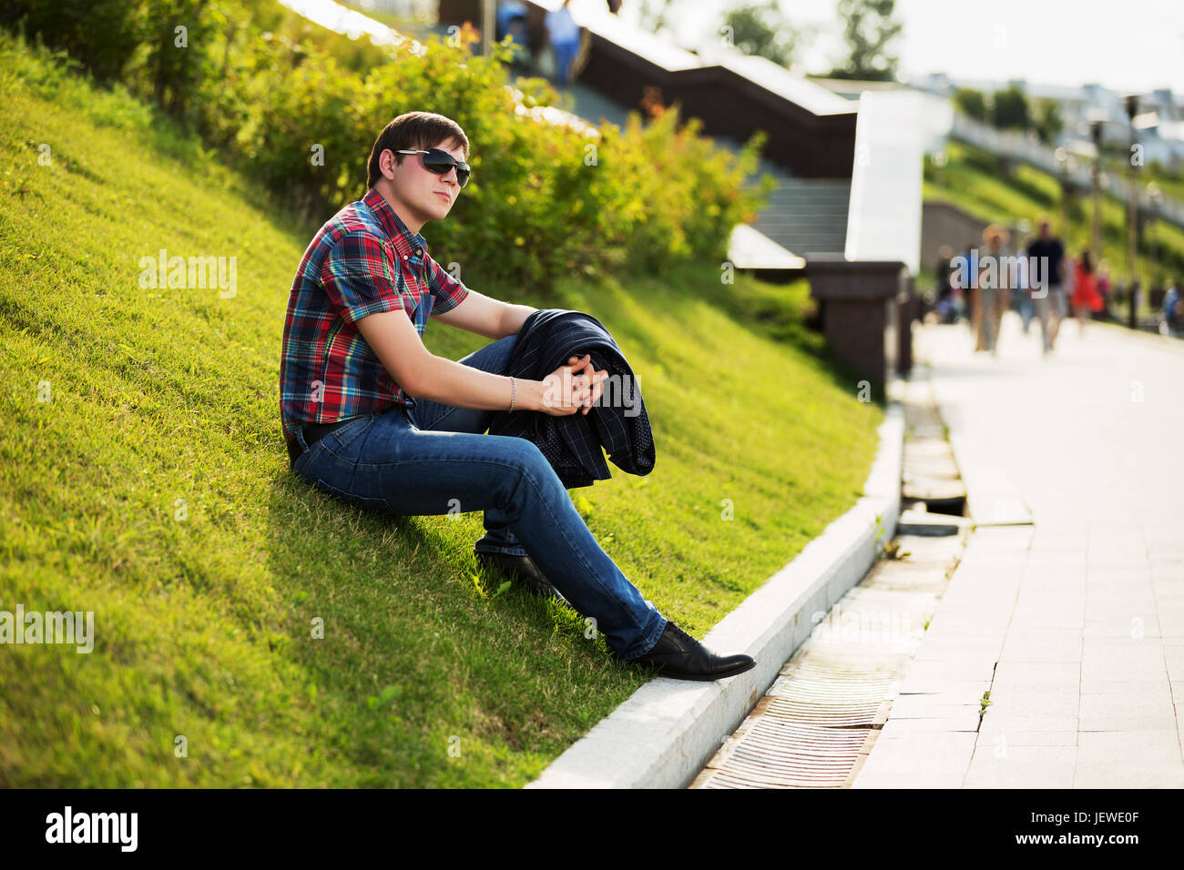 Young fashion man in sunglasses sitting on the grass in a city park Stock Photo