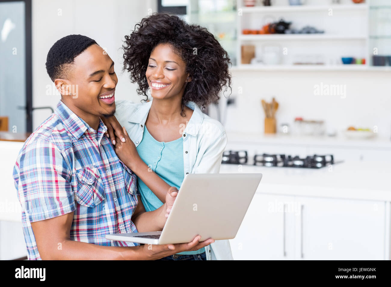 Happy young couple using laptop in kitchen Stock Photo - Alamy