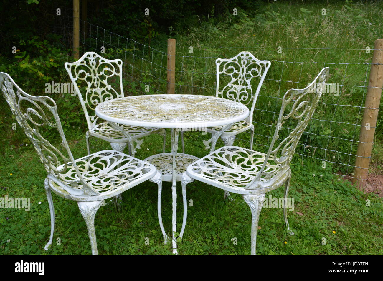 Weathered Ornate Scrolled Aluminium White Painted Round Garden Table And Chair Set On Lawn With Wire Mesh Boundary Fence Meadow Grass In Background Stock Photo Alamy