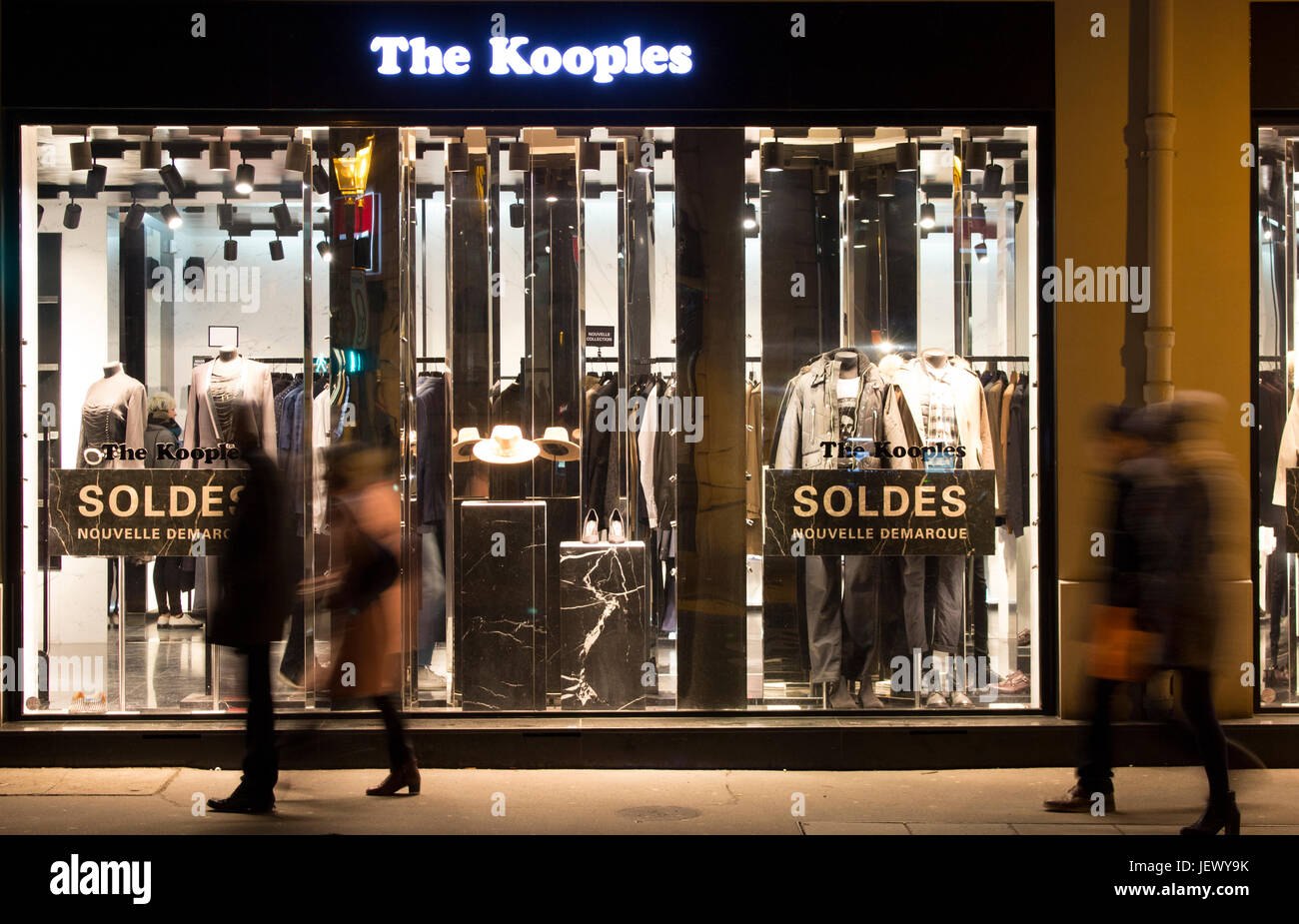 View of people walking in blurry motion in front of fashion brand store at night in Le Marais district of Paris. Sale season and consumerism concept. Stock Photo