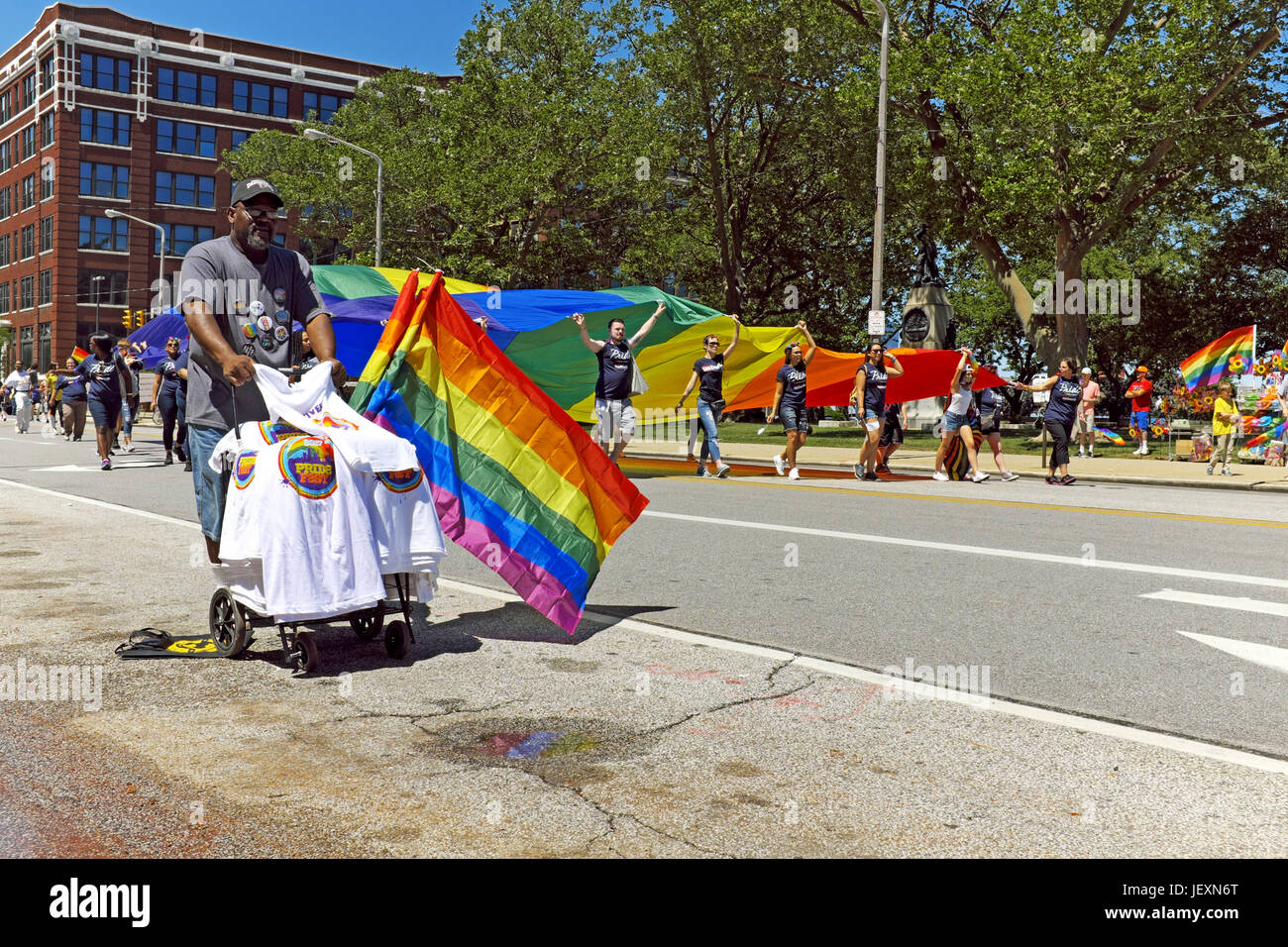 Vendor selling LGBT pride 2017 T-shirts and flags along the parade route in downtown Cleveland, Ohio, while a large rainbow flag is carried by. Stock Photo