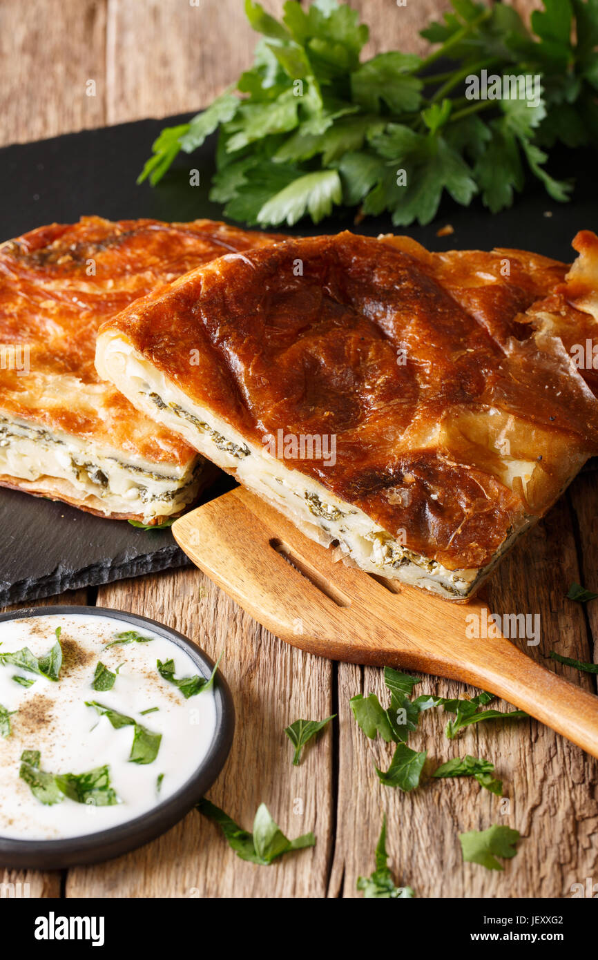 Burek stuffed with spinach and cheese and with sour cream sauce close-up on the table. vertical Stock Photo