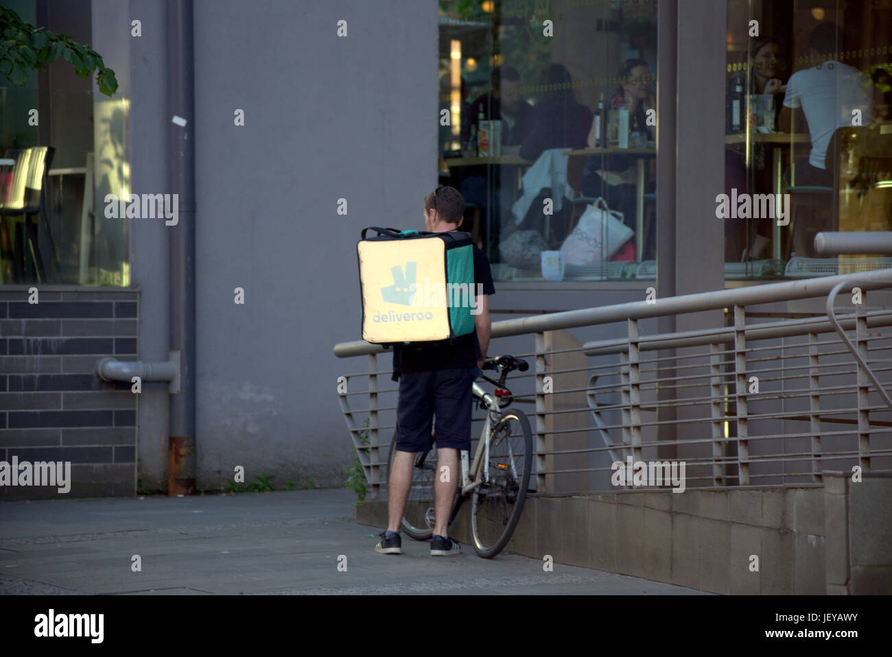 young man boy delivery bike cyclist Deliveroo food delivery texting waiting for job delivering outside restaurant Stock Photo