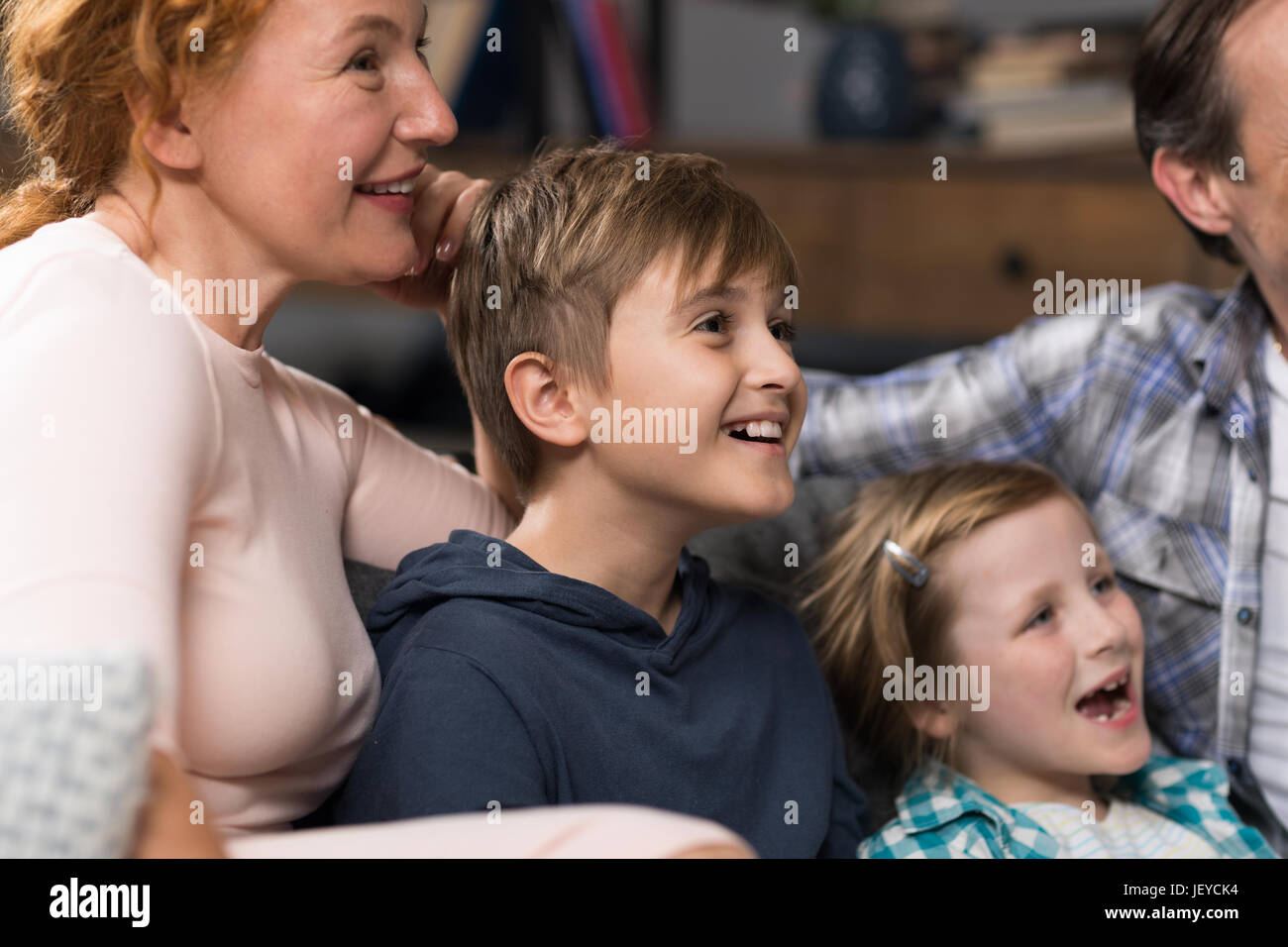 Closeup Of Happy Smiling Family Sitting On Couch Watching TV, Parents Spending Time With Children In Living Room Stock Photo