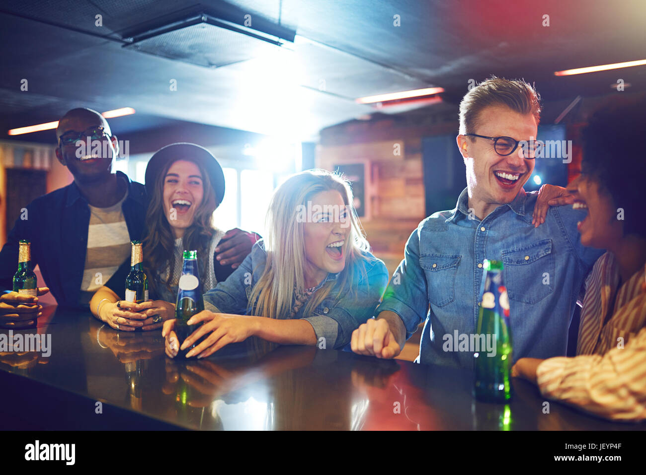 Horizontal shot of cheerful laughing people sitting at the bar counter and having a beer. Stock Photo