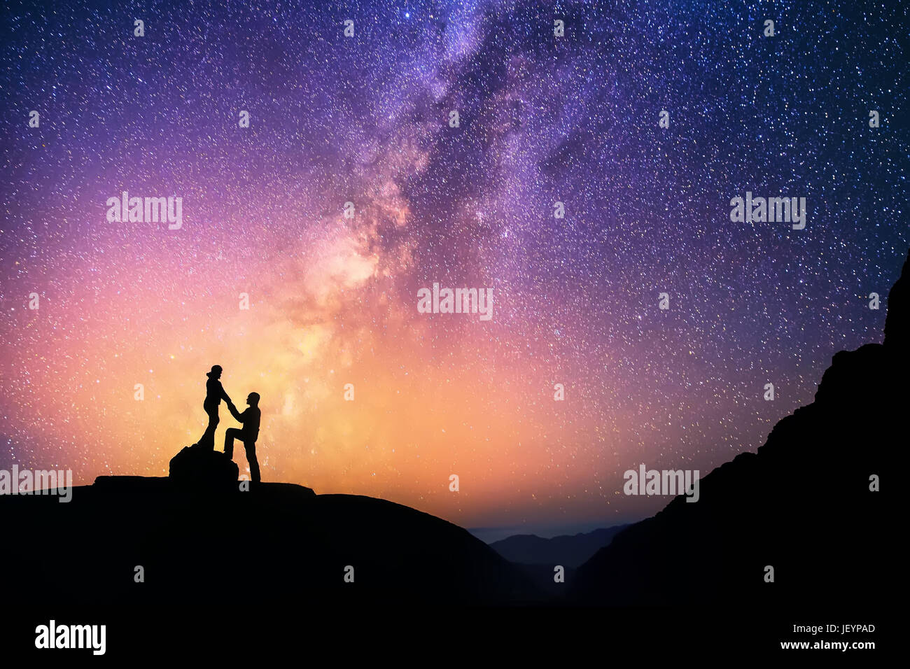 Romantic couple standing together holding hands in the mountains. Beautiful Milky Way galaxy on the background. Stock Photo