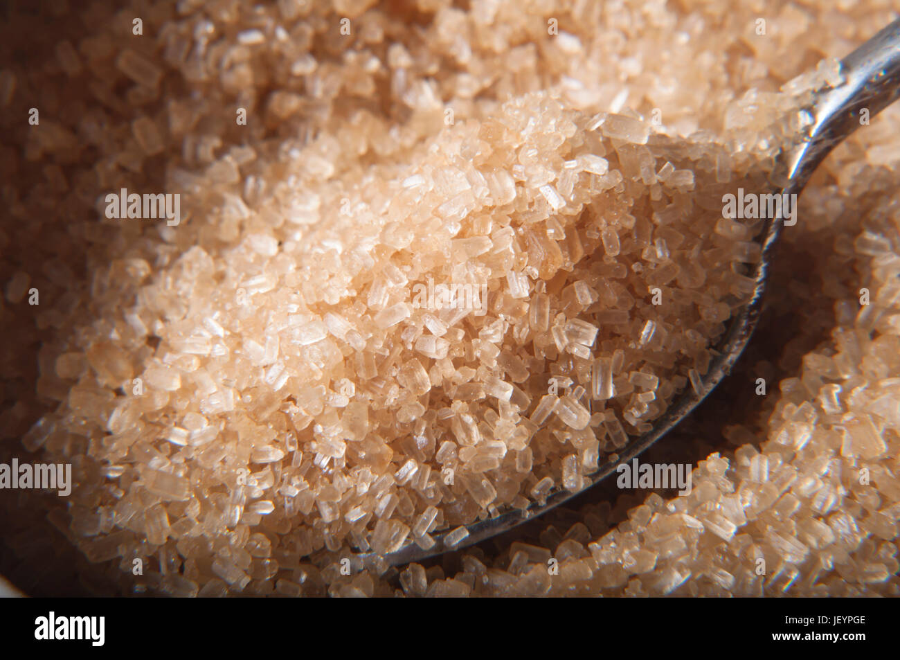 Close up (macro) shot.  A spoon filled with brown raw cane (demerera) sugar granules being lifted from bowl.  Selective focus. Stock Photo