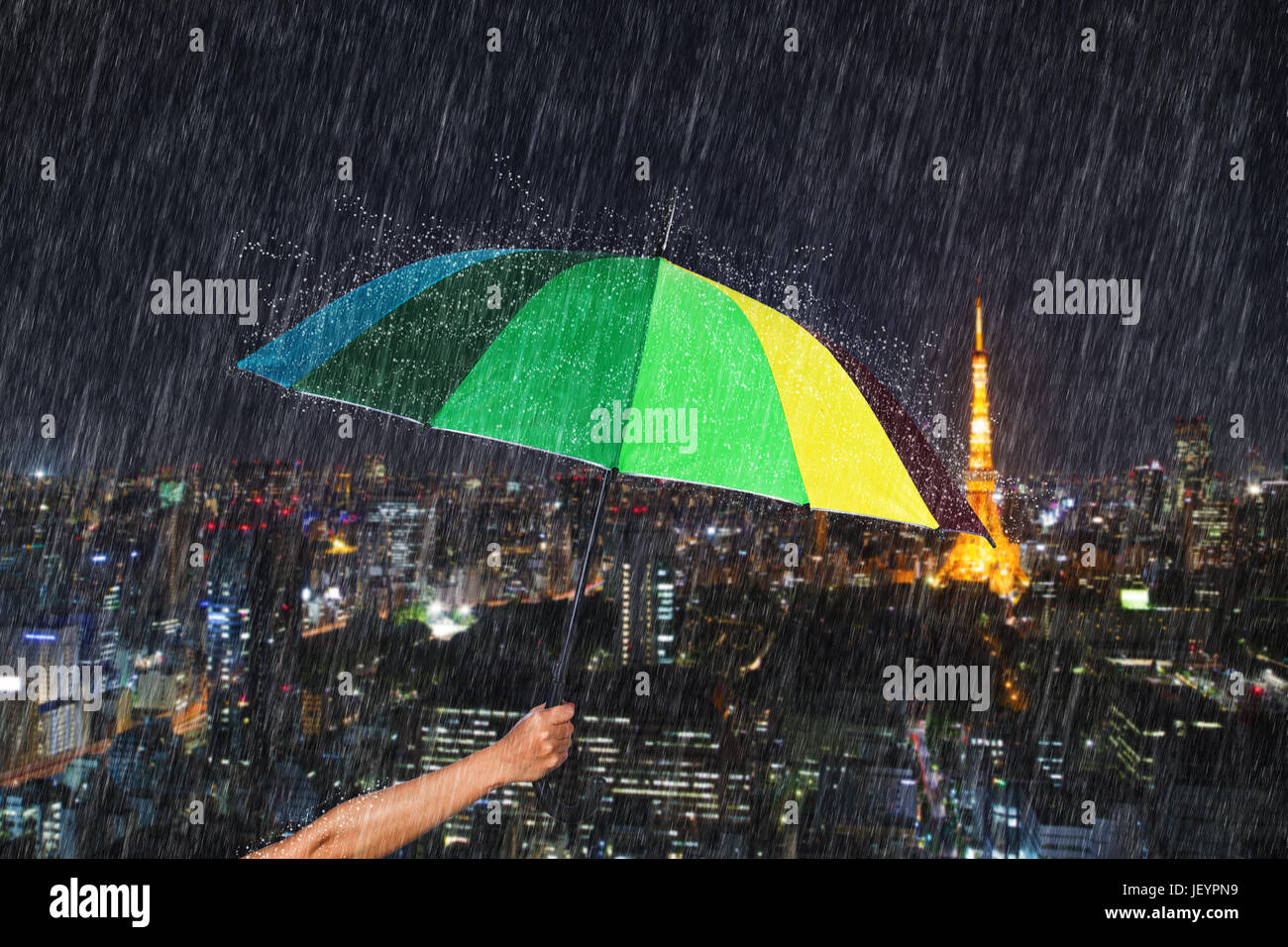 hand holding multicolored umbrella with falling rain at Tokyo city background, Japan Stock Photo