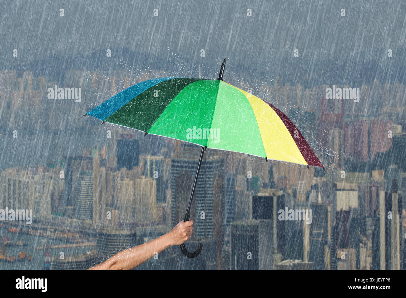 hand holding multicolored umbrella with falling rain at Hond Kong city background Stock Photo
