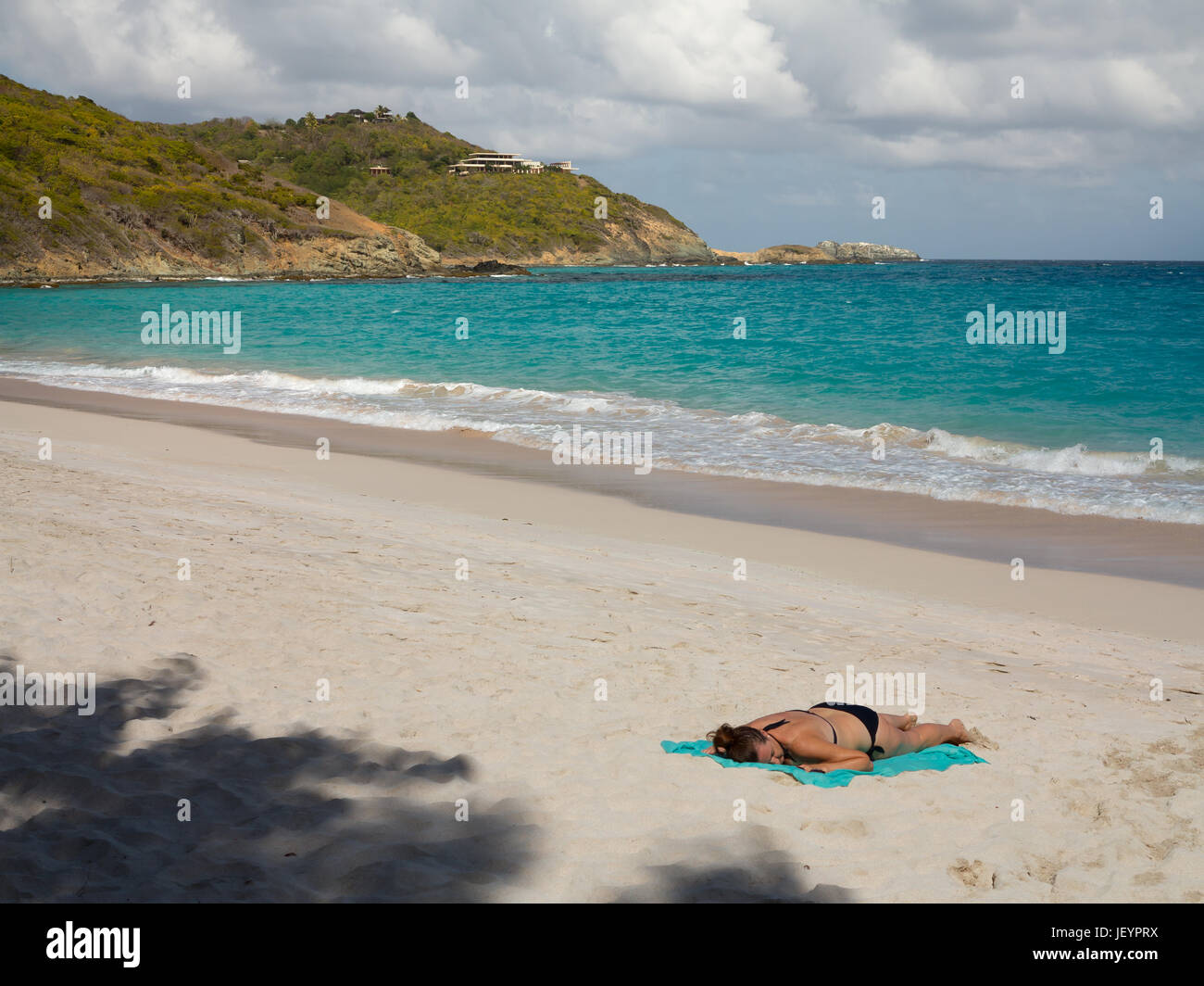 A woman sunbathing on Macaroni Beach Mustique, A white sand pristine beach with Azure Blue water