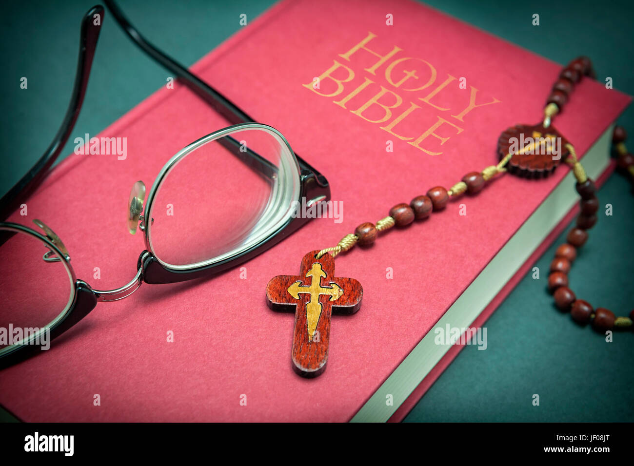 Glasses adjusted on the holy bible and beads on green background Stock Photo