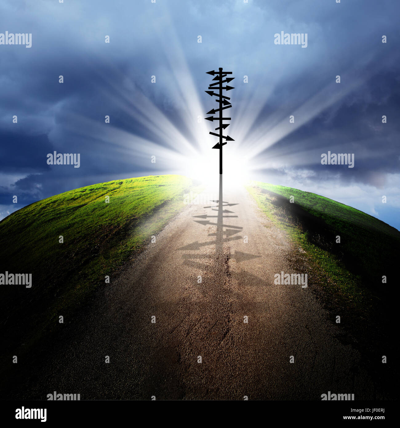 conceptual image of silhouetted directional sign on empty road over cloudy sky with beam of light Stock Photo