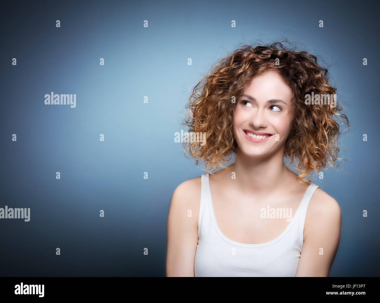 Cute, authentic girl portrait on grey and blue background. Young woman smiling, looking up. Stock Photo