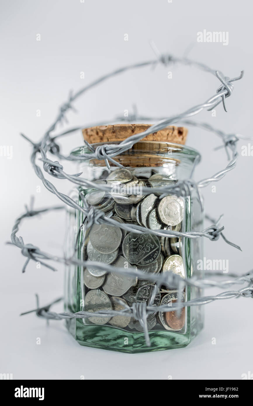 Jar half full of money surrounded with barbed wire. Stock Photo