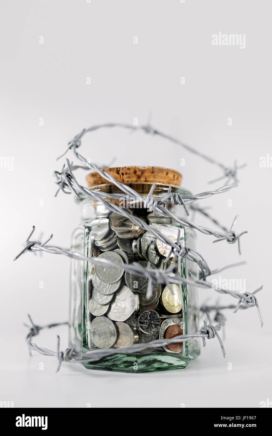 Jar half full of money surrounded with barbed wire. Stock Photo