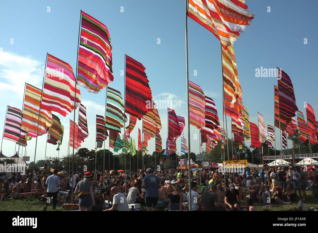People sitting beneath colourful flags near the West Holts Stage at Glastonbury Festival, Pilton, Somerset, England, United Kingdom, June 2017. Stock Photo