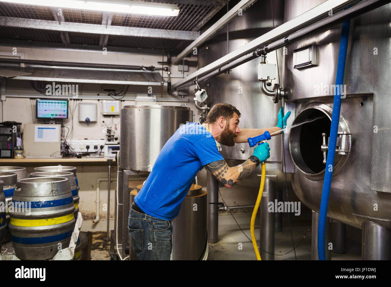Man working in a brewery, cleaning inside of a large stainless steel kettle with a high pressure washer. Stock Photo