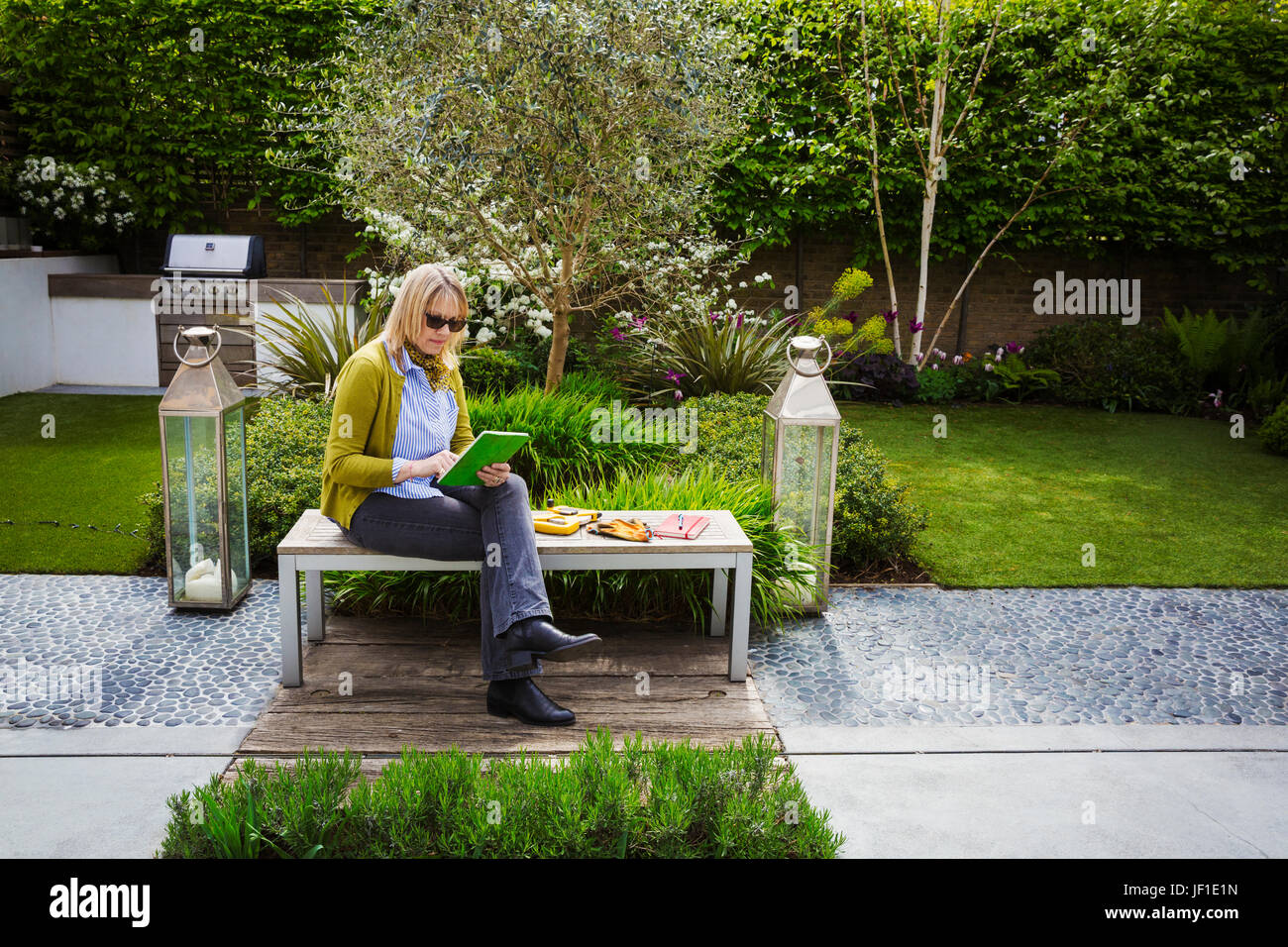 Woman sitting on a bench in a garden, drawing flowers in a sketchbook. Stock Photo