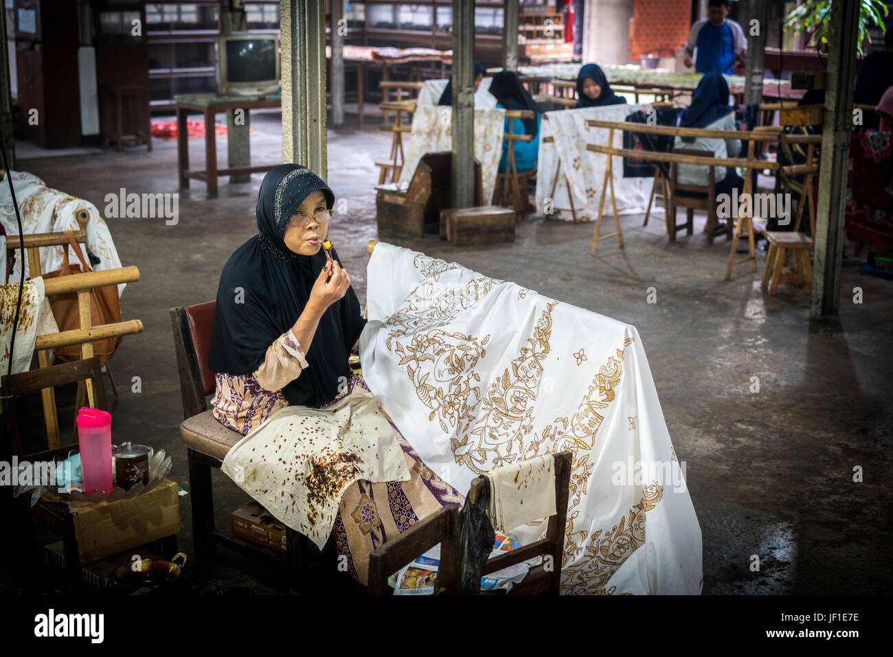 Several people working in a batik workshop in Indonesia. Woman in the foreground is applying wax to the design. Stock Photo