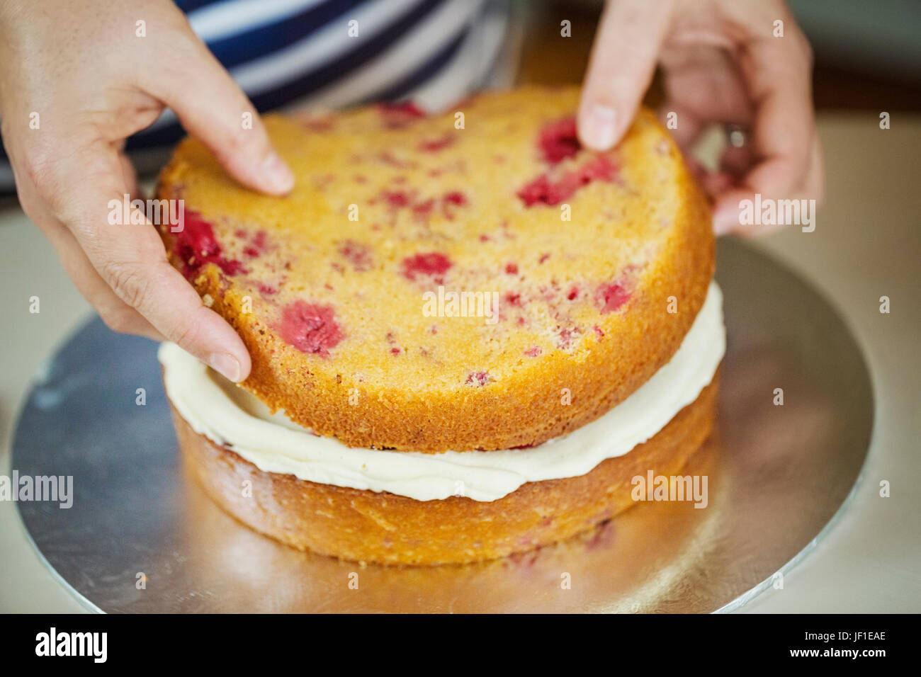 Close up high angle view of person assembling a layer cake, placing top on layer of cream. Stock Photo