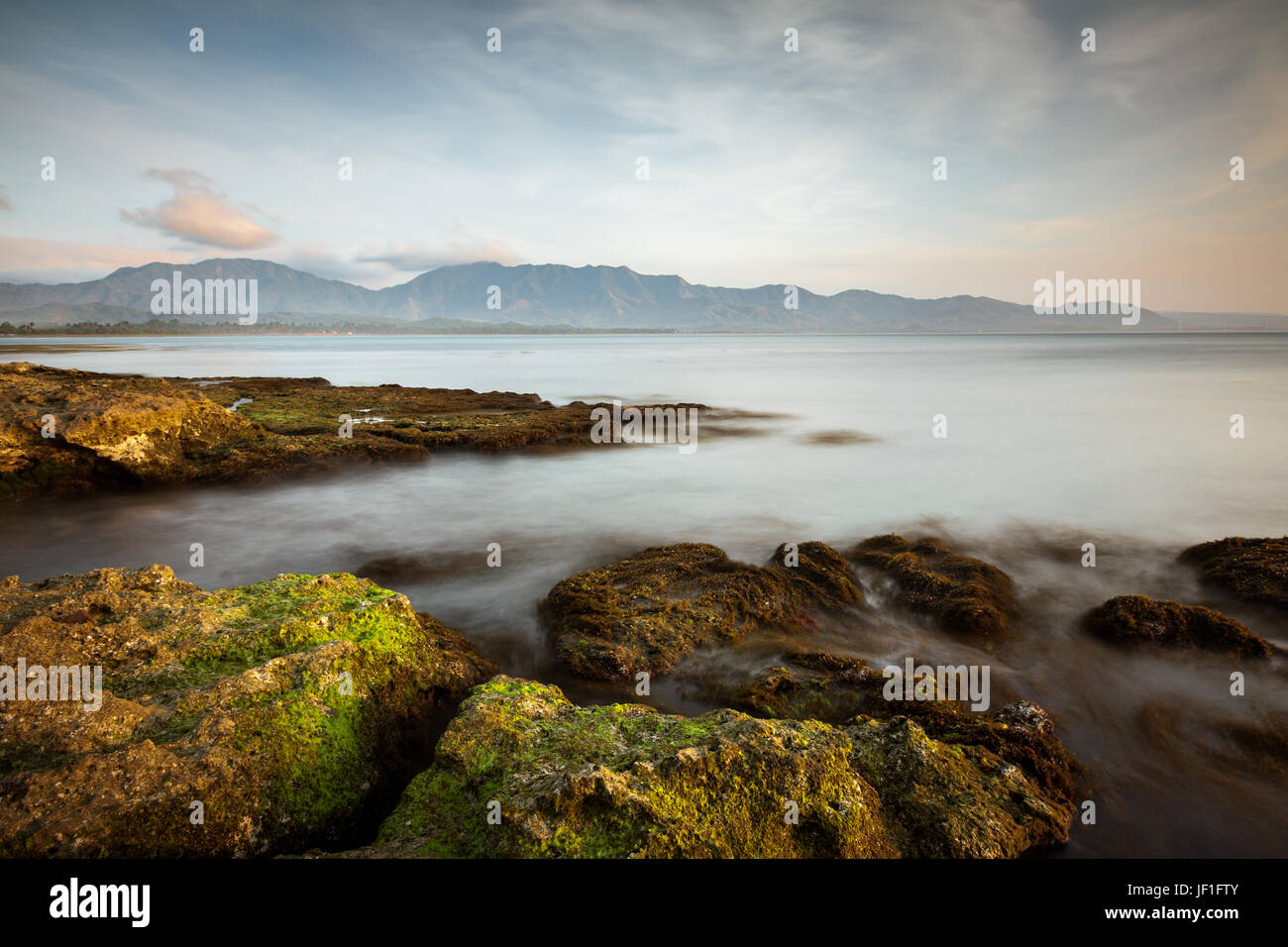 Stunning dramatic seascape photo of rocky coastline. An idyllic long exposure seascape image with a beautiful mountain background in the Philippines Stock Photo