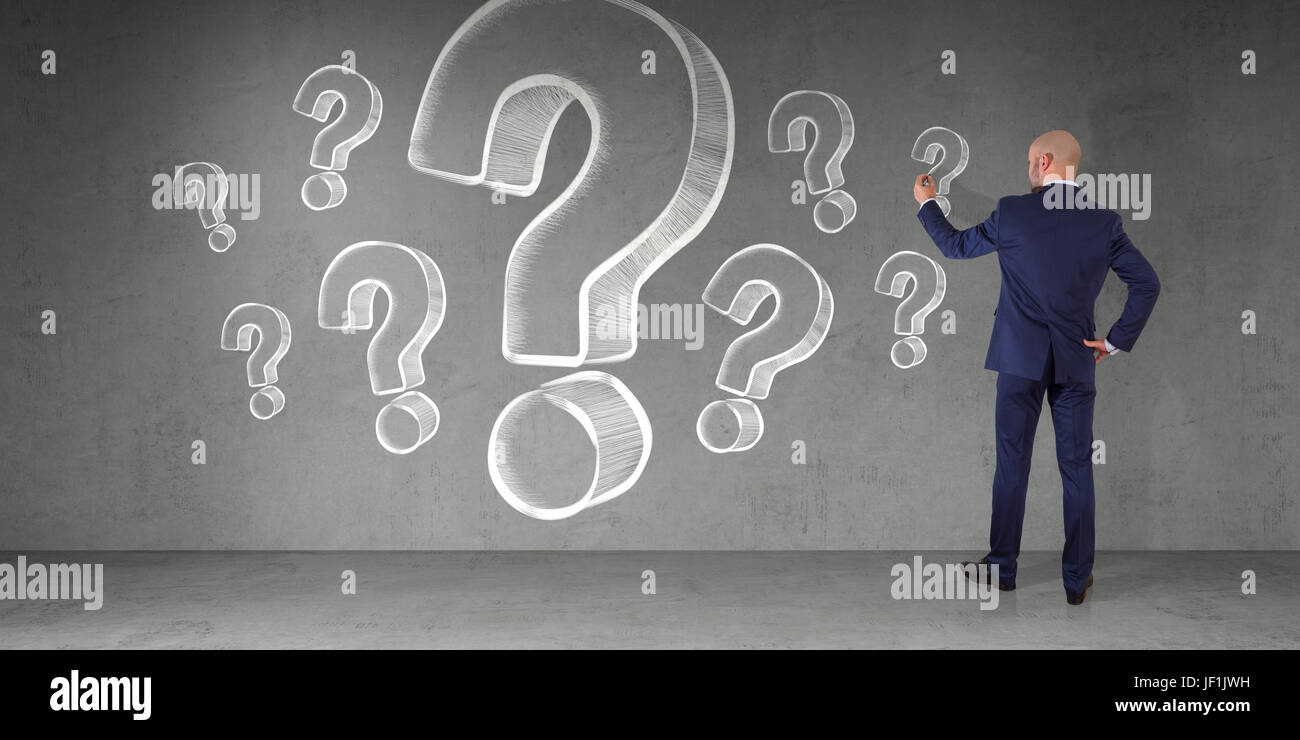 Businessman in modern interior drawing question marks sketch on a wall ...