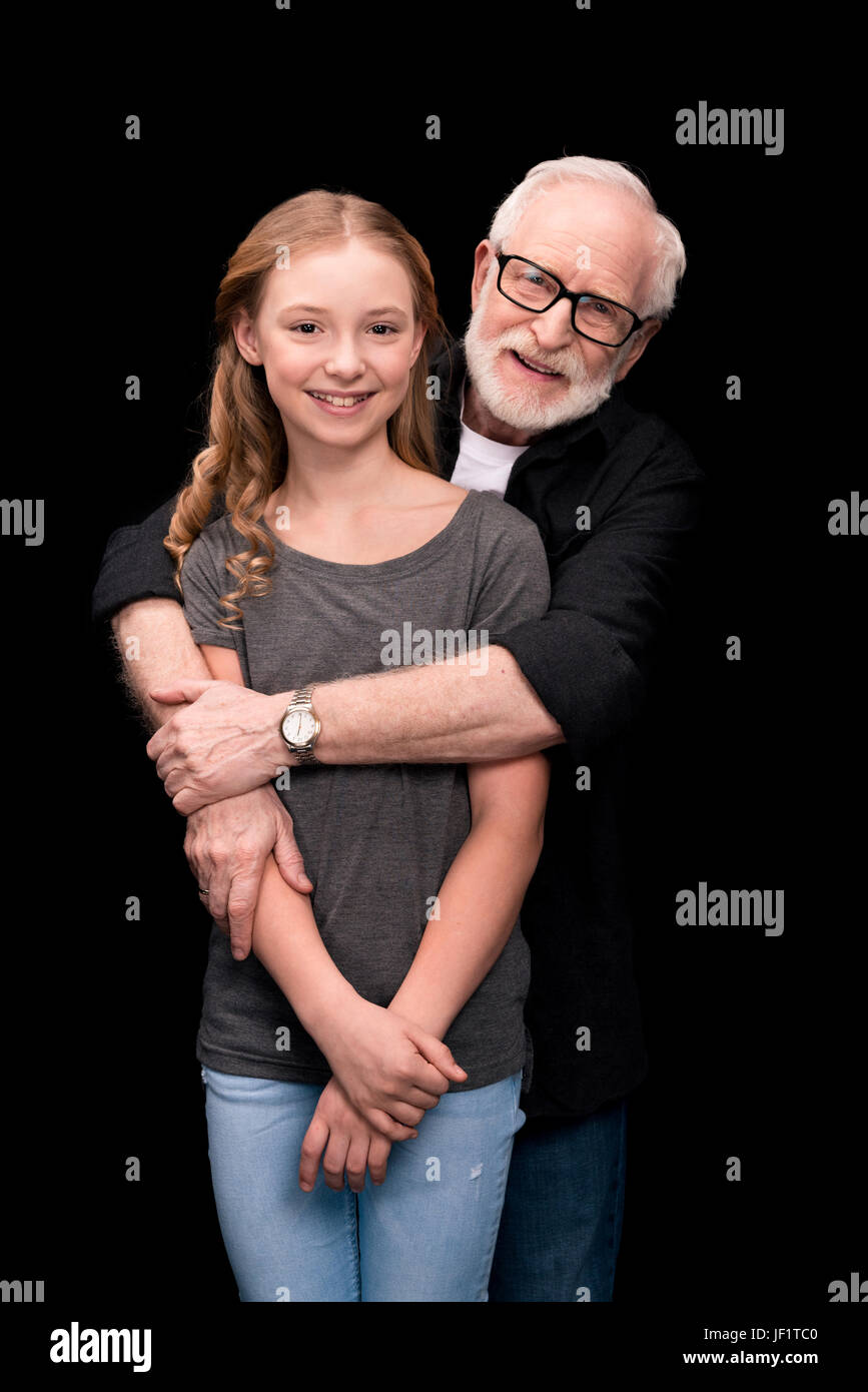 smiling grandfather hugging teenage granddaughter isolated on black ...