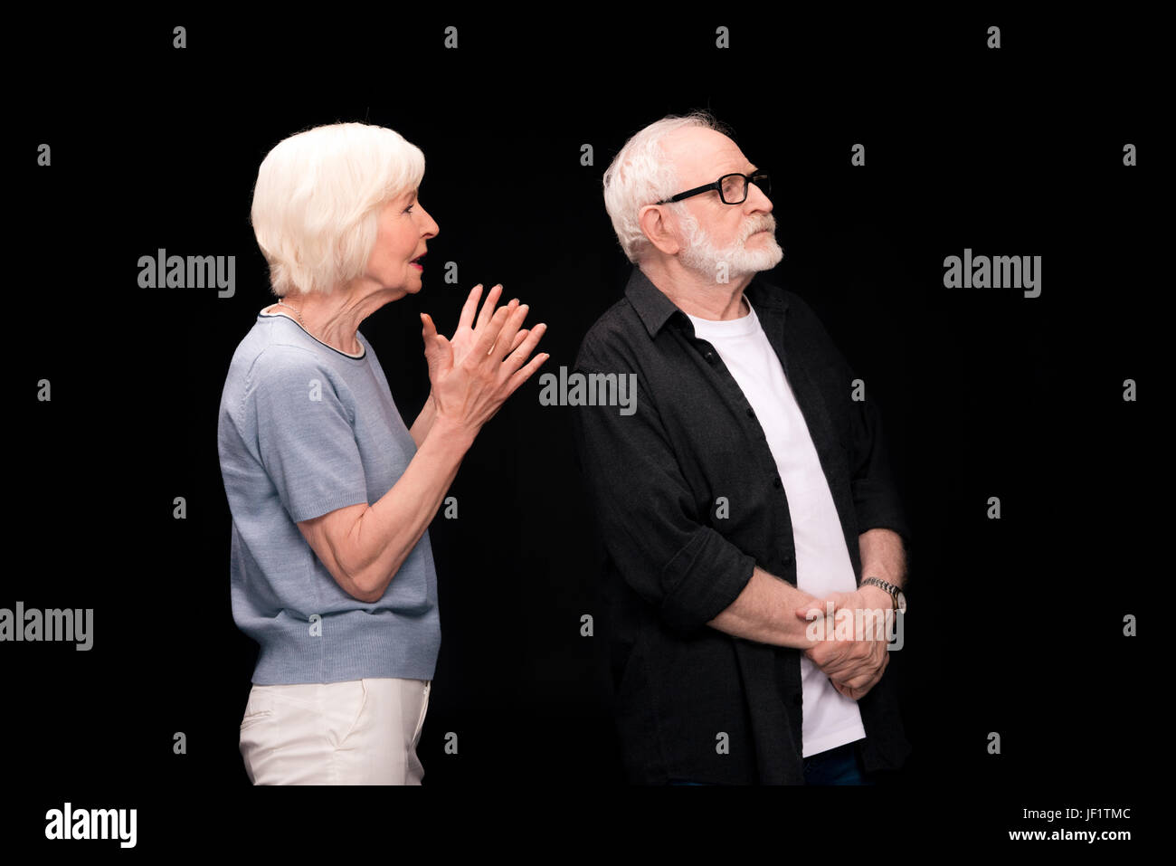 Serious senior couple standing and arguing isolated on black Stock ...