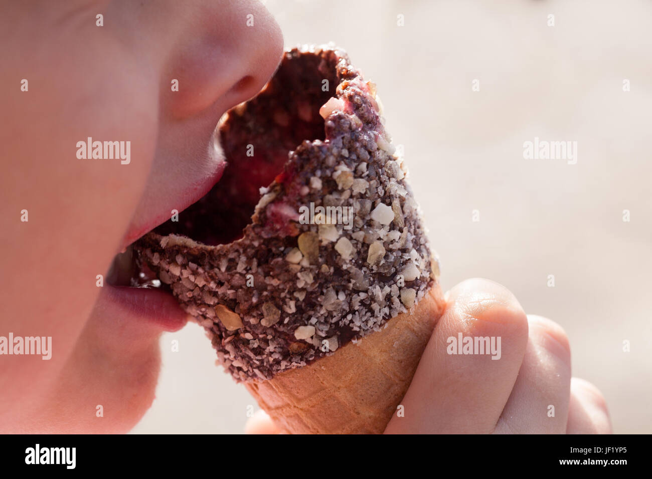 Close up of a child's face and hand eating an ice cream waffle cone covered in chopped nuts and chocolate. Summer theme image. Stock Photo