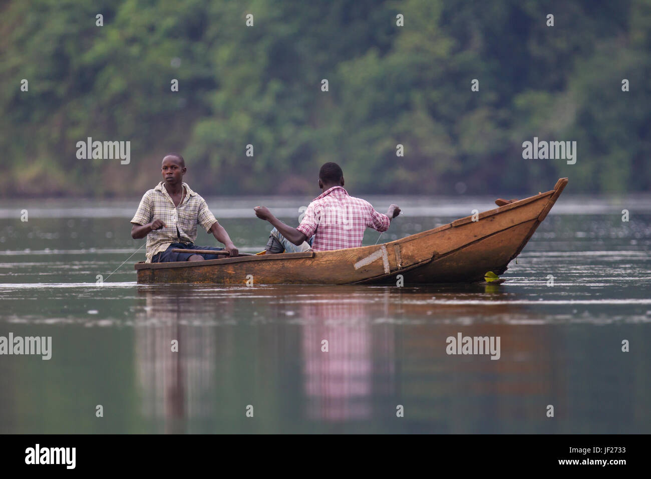Two men fish by hand from a small wooden boat at the source of the Nile River, Jinja, Jinja District, Uganda. Stock Photo