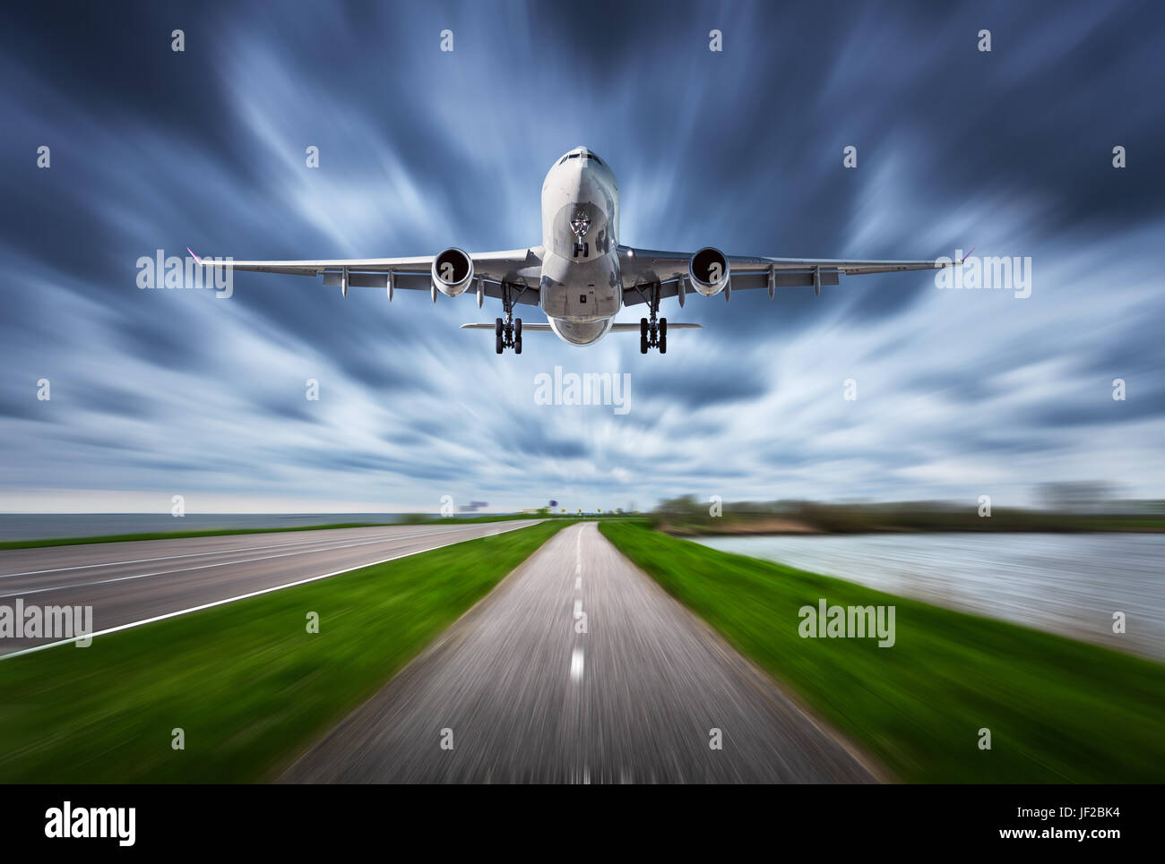 Airplane and road with motion blur effect. Landscape with white passenger airplane is flying in the cloudy sky over the asphalt road. Blurred. Passeng Stock Photo