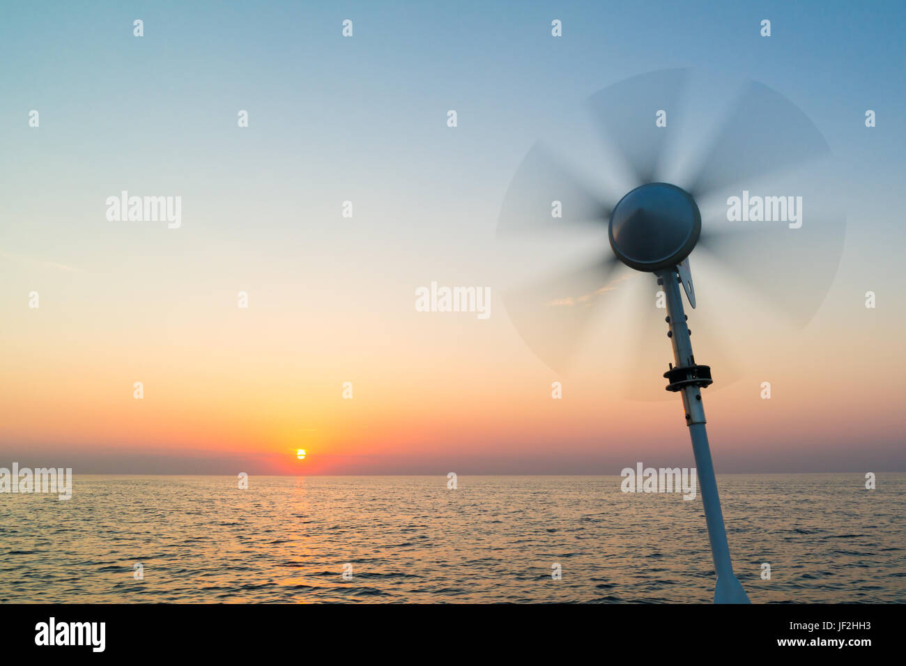 Marine wind turbine on sailing boat with turning blades using wind power to charge onboard batteries on North Sea at sunset, Netherlands Stock Photo