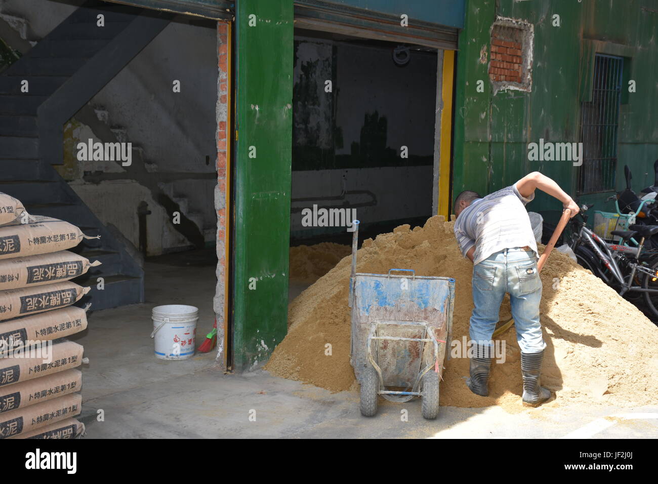 Man digging up sand to mix into cement to repair an old building in Taiwan. This means the new renters payed to have it done before opening. Stock Photo